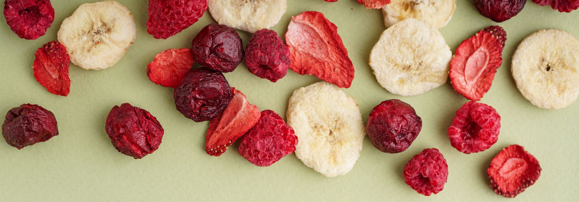 Mélange de fruits lyophilisés Wellioo (banane, fraise, framboise, cerise) sur fond vert sauge.